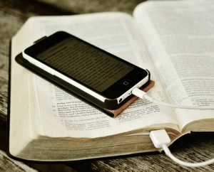 A picture of an open Bible with a smart phone open to a photo of the open Bible's page and a phone charging cord.