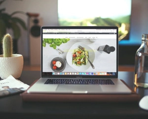 Photo of a desk with a laptop open to a website displaying a salad and yogurt with fruit.