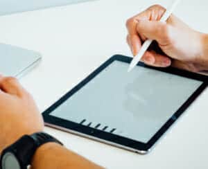 A picture of a tablet on a desk with two hands using a tablet pencil simulating drawing. 