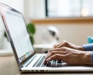 Picture of persons hands resting on a laptop keyboard while on a desk.