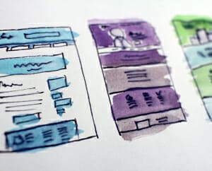 Picture of a sketch pad with website landing page concepts drawn in blue, purple, green, and black.