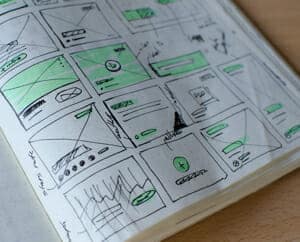 Picture of a sketchbook with green and black doodles depicting a website layout plan.