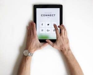 This is a picture of a man's arms and hands holding a tablet with a screen displaying the words CONNECT and six social media graphics in a two by three grid.