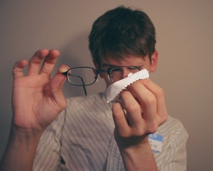 Picture of a man cleaning his glasses with a cleaning cloth.