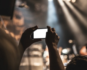 Picture of hands holding a smartphone in landscape mode taking a video of a band.