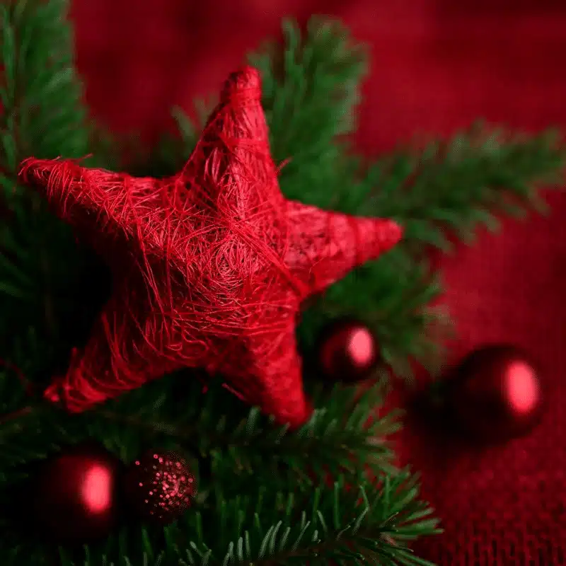 Picture of red star on a section of a green Christmas tree with red glass balls hanging from the tree.