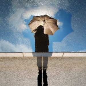 A graphic of a woman's reflection holding an umbrella with a blue sky with white clouds and the pavement under her feet.