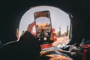 A picture of someone gazing out of a tunnel with a background of nature and a smartphone opened in the camera app to take a picture. 